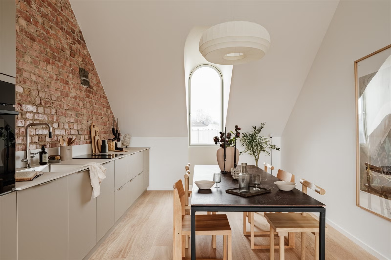 Attic kitchen and dining area with arched window and exposed brick in the Living Under the Sky apartment in Oslo by IK-architects